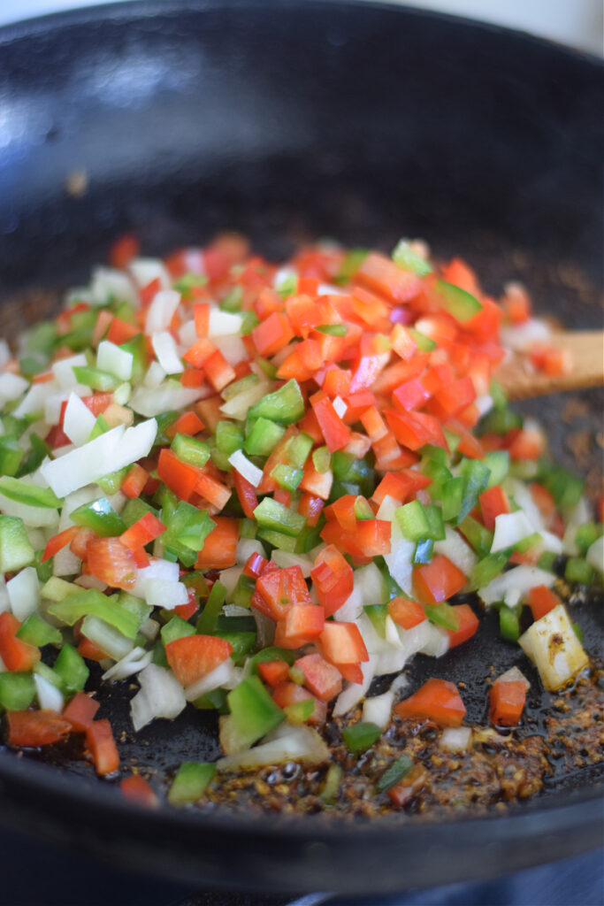 Diced peppers and onions in a skillet.