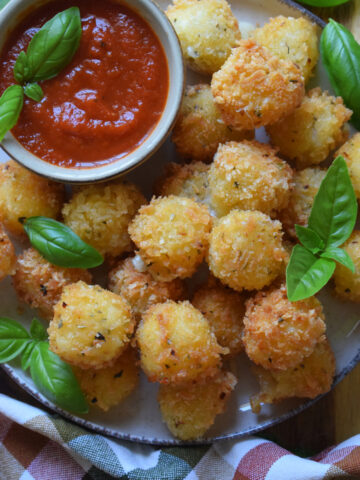Panko crusted cheese on a plate with marinara sauce and basil.