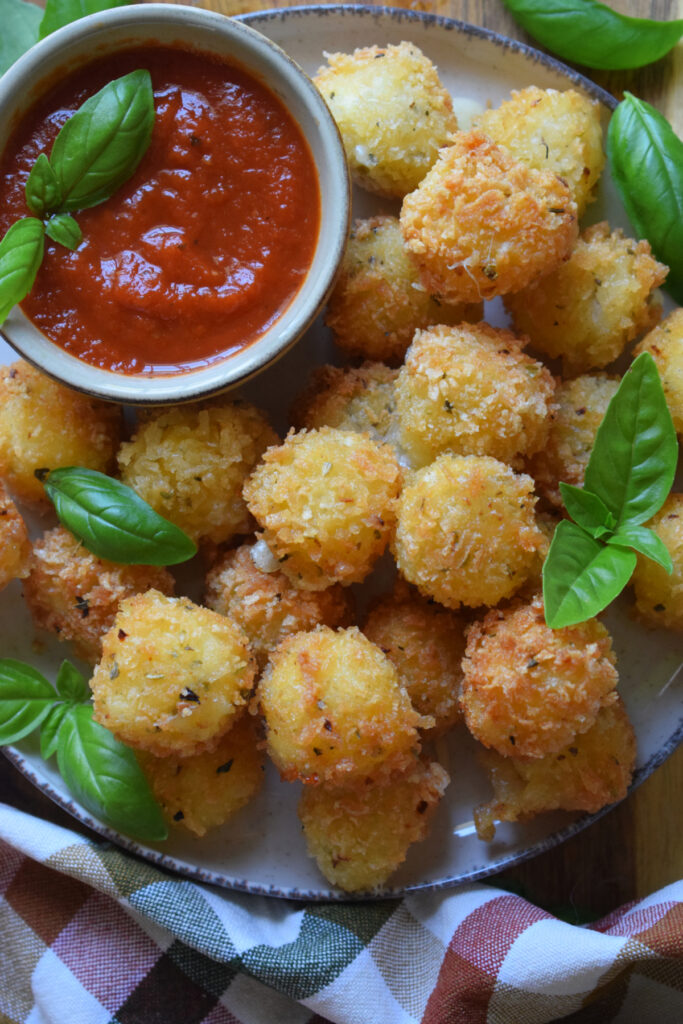 Panko crusted cheese on a plate with marinara sauce and basil.