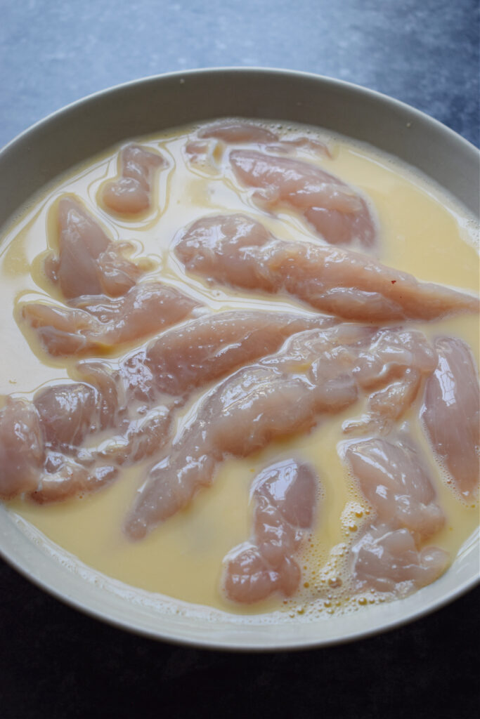 Coating chicken tenders in whisked eggs.