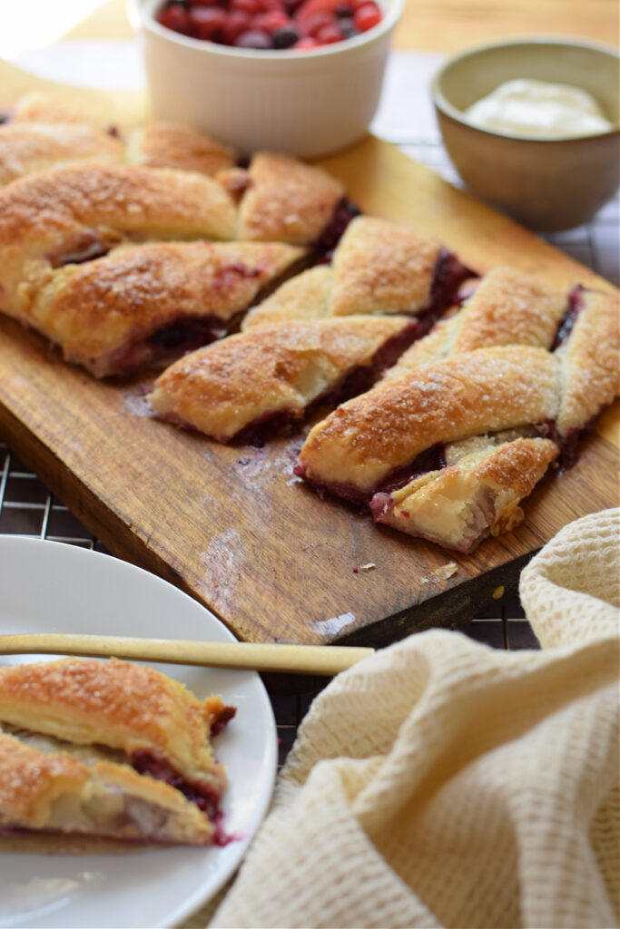 Berry cream cheese danish on a board and a slice on a small plate.