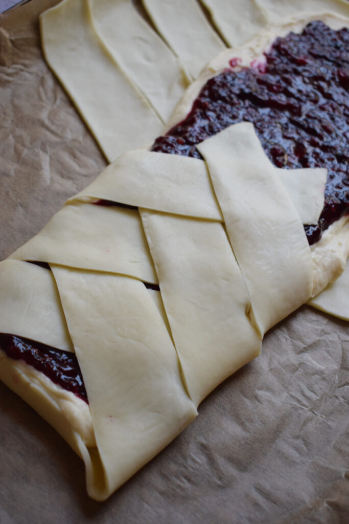 Folding pastry strips over berry filling. in a danish.