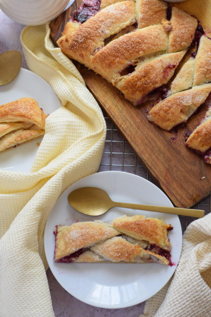 Berry cream cheese danish on a board and a slice on a plate.