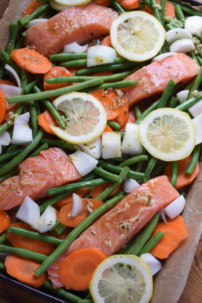 Marinade poured over salmon and vegetables on a large baking tray.