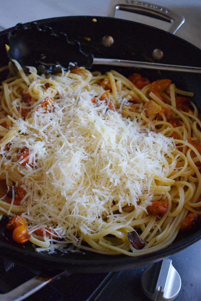 Adding parmesan cheese to pasta in a skillet.