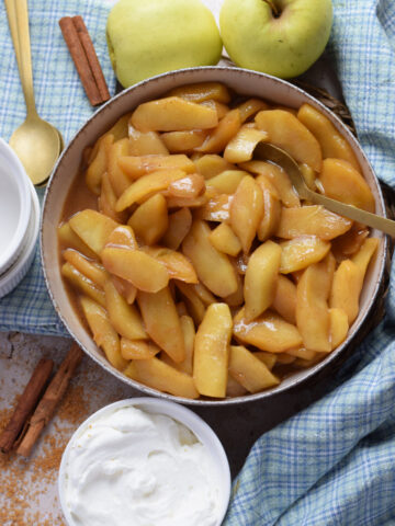 Caramelized apples in a bowl with whipped cream.