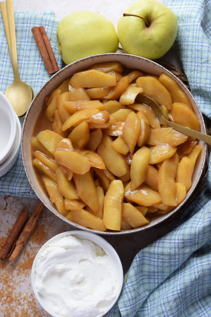 Caramelized apples in a bowl with whipped cream.