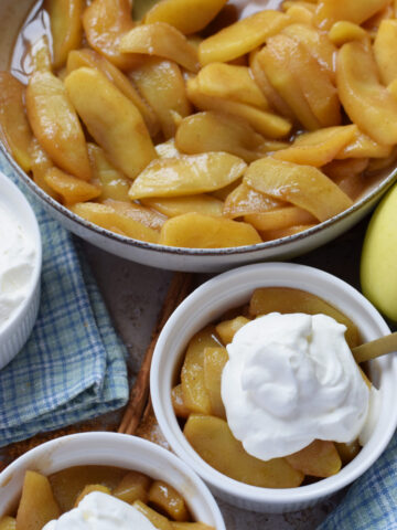 Caramelized apples in bowls with whipping cream.