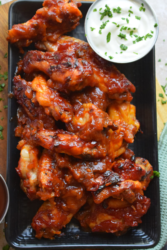 Chicken wings on a black plate with a dip.