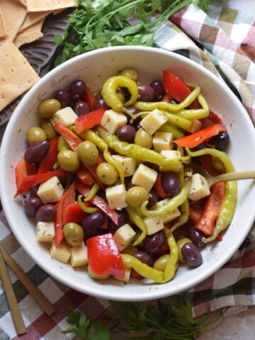 Marinated olives and cheese in a white bowl.