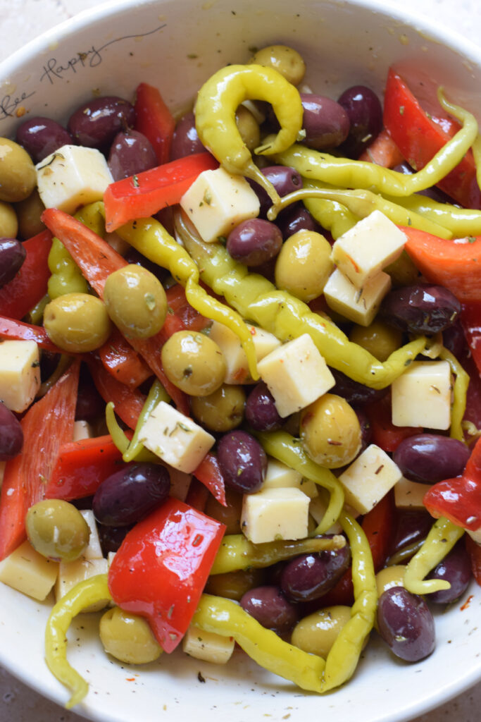 Antipasto olives and cheese mix in a white bowl.