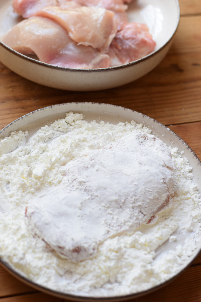 Dredging chicken in corn flour.