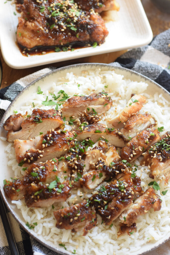 Slices of soy ginger chicken served over white rice on a plate.