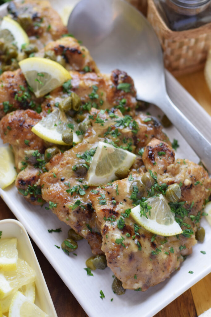 Chicken cutlets on a white plate with lemon and capers.