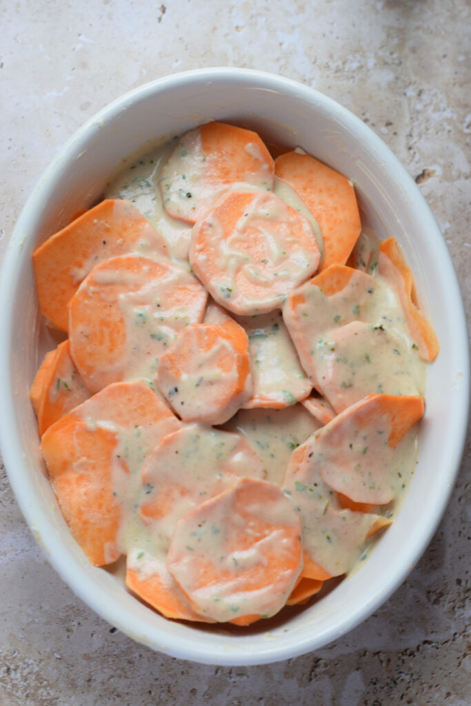 Pouring sauce over sliced sweet potatoes.