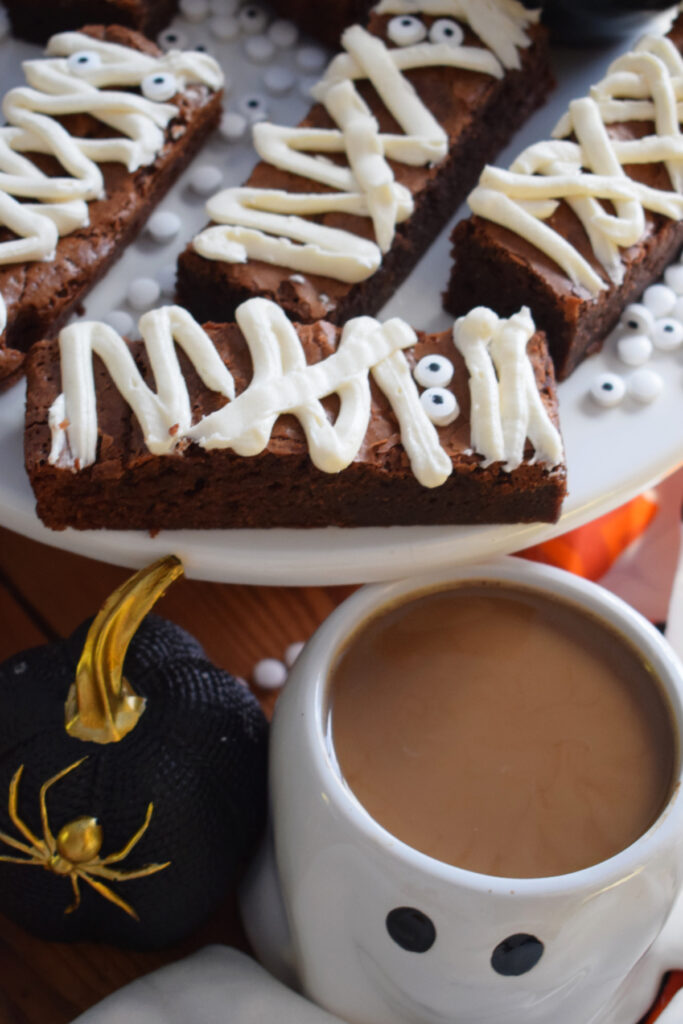 Chocolate mummy brownies on a tray with a cup of coffee.