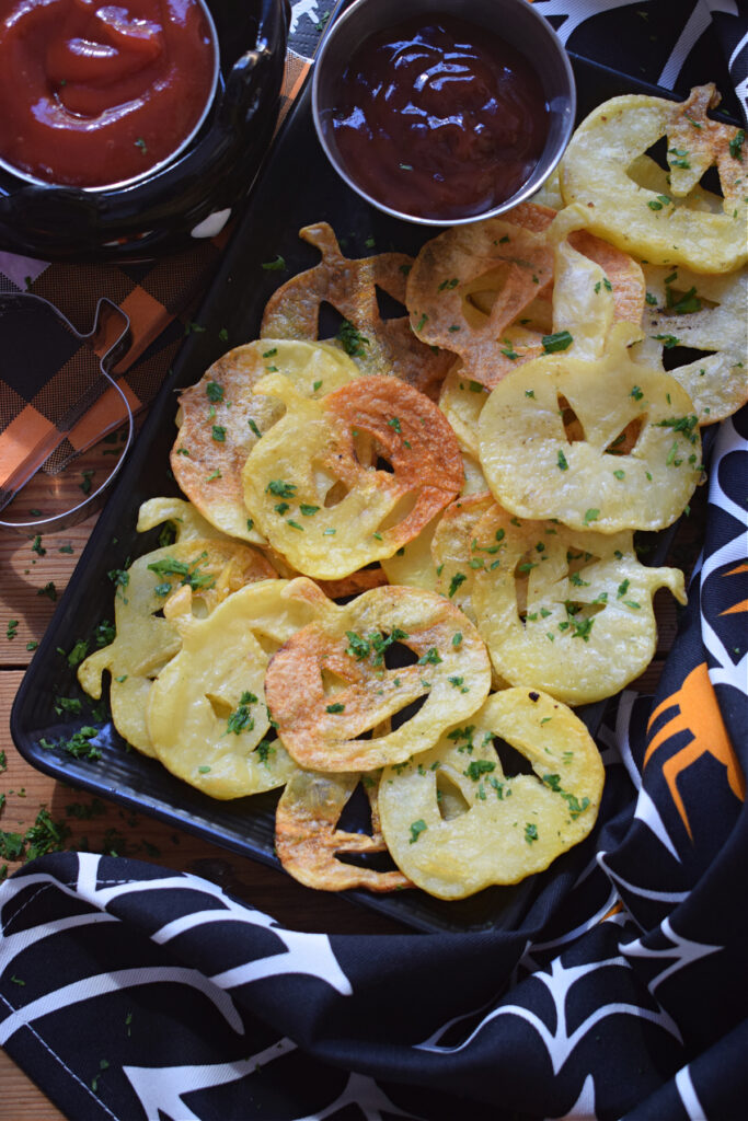 Halloween style potato chips on a black plate.