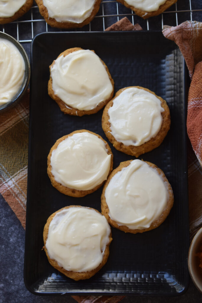 Frosted pumpkin cookies on a black plate.