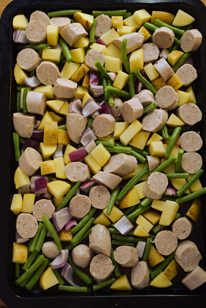 Vegetables and sausages on a large baking tray.