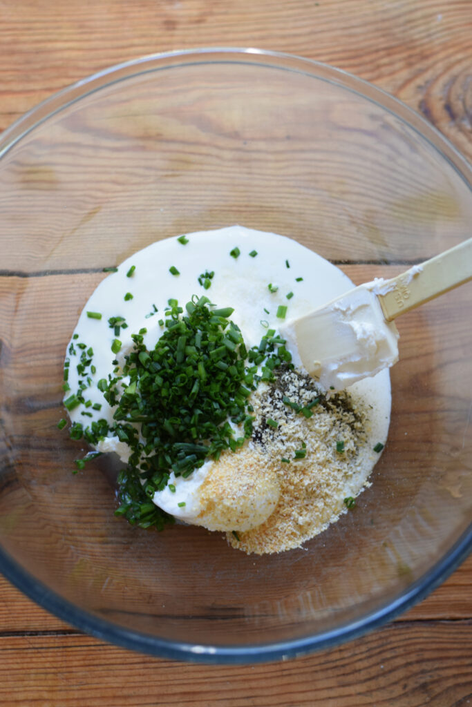 Ingredients in a glass bowl to make sour cream and chive dip.