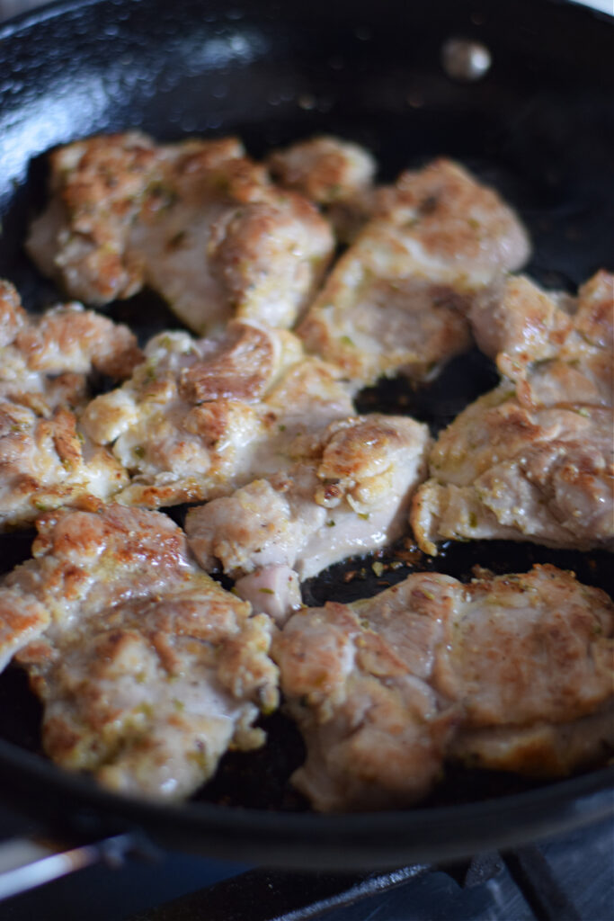 Chicken cooking in a cast iron skillet.