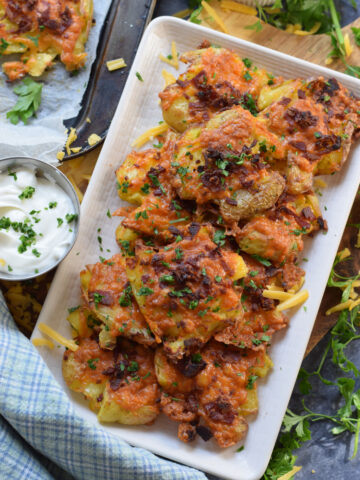 Smashed potatoes with cheese and bacon on a white plate.