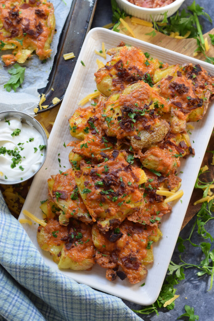 Smashed potatoes with cheese and bacon on a white plate.