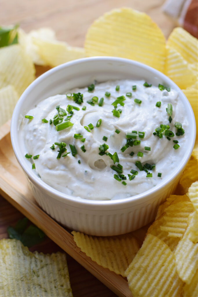 Dip with chives in a white bowl with chips on the side.