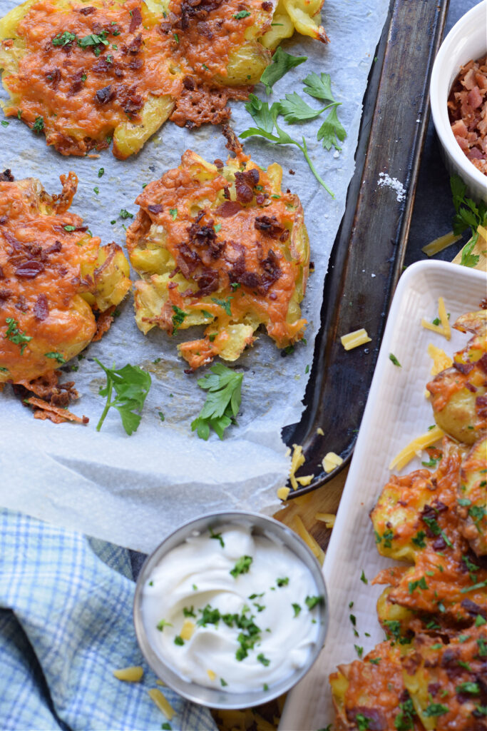 Bacon cheese smashed potatoes on a baking tray with dipping sauce.