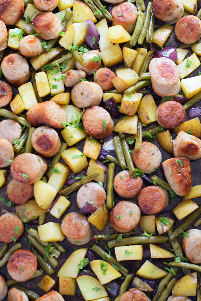 Pork sausages and potatoes on a sheet pan.