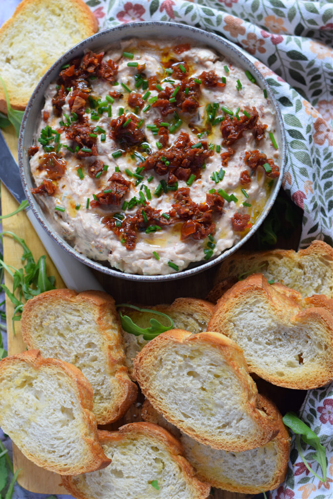 Sun dried tomato dip with baguette slices on a platter.