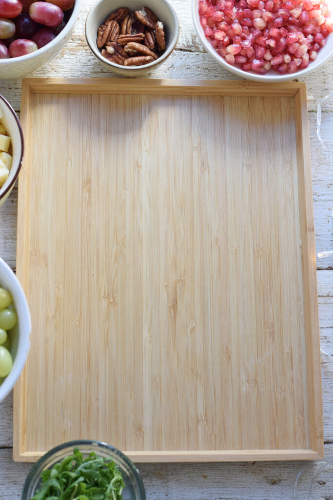 A wooden board with bowls of fruit and cheese.