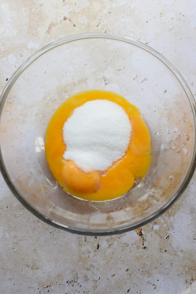 Adding egg yolks and sugar to a mixing bowl.