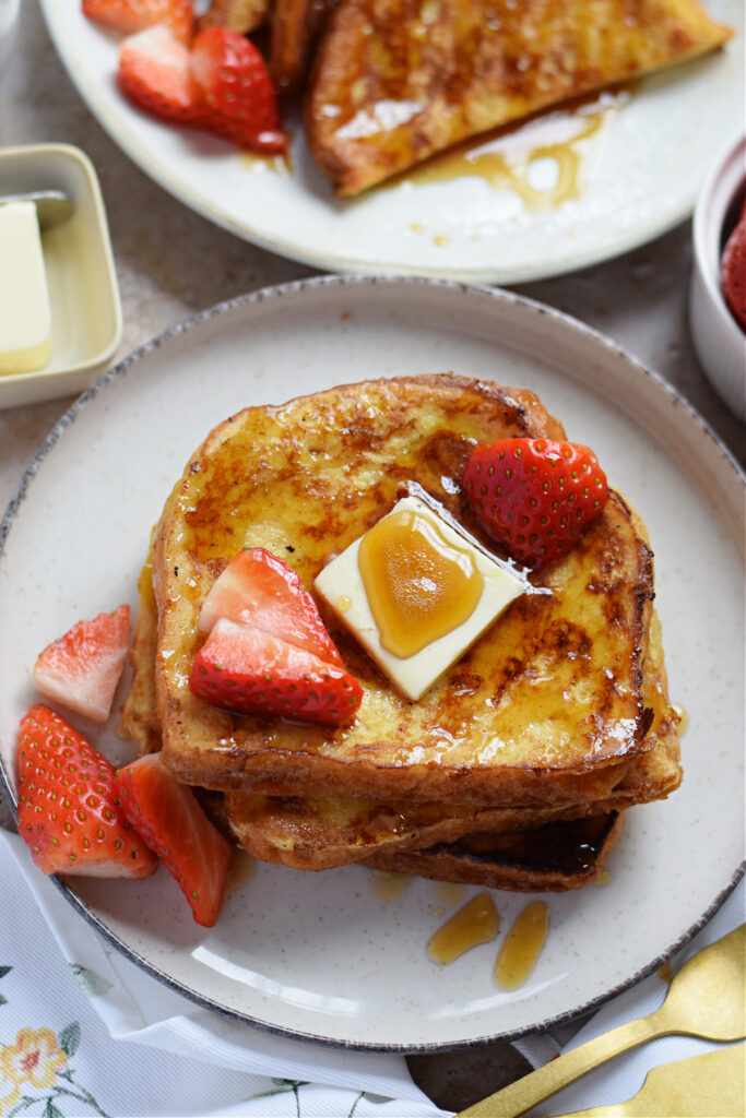 French toast served on a plate with butter, berries and maple syrup.