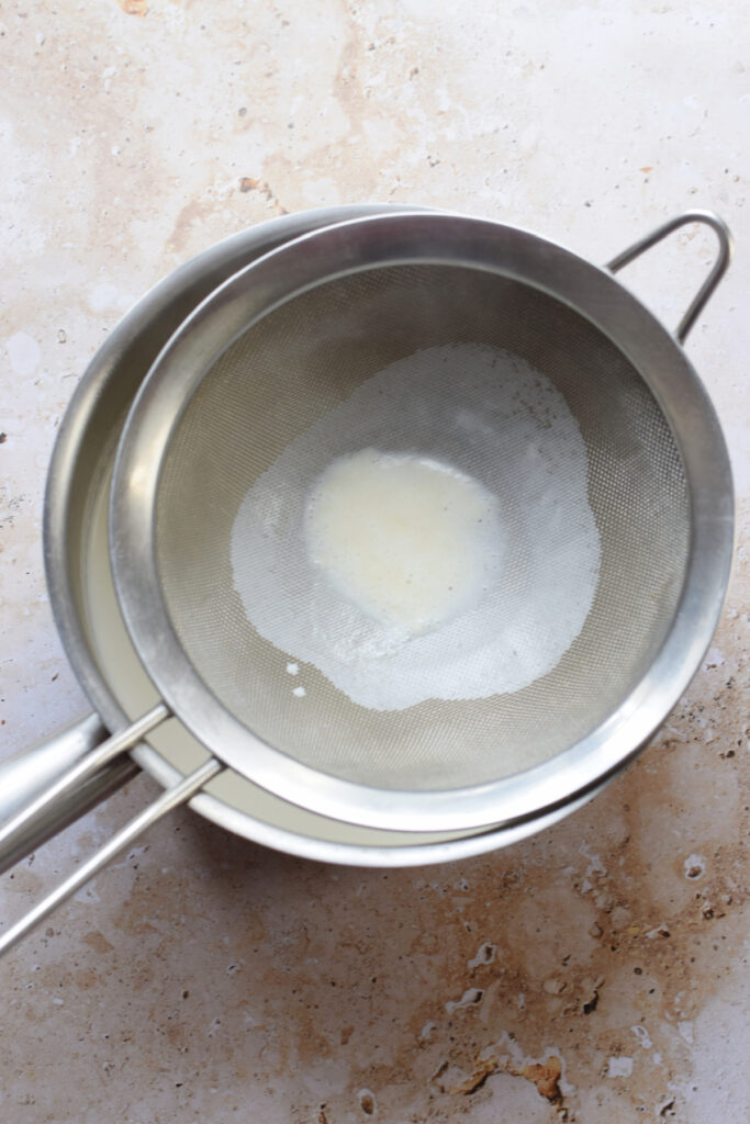 Straining cream through a mesh strainer.