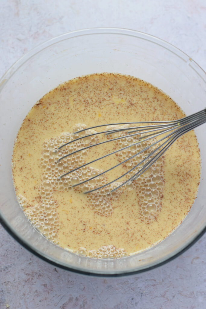 Whisking together eggs and milk in a glass bowl.