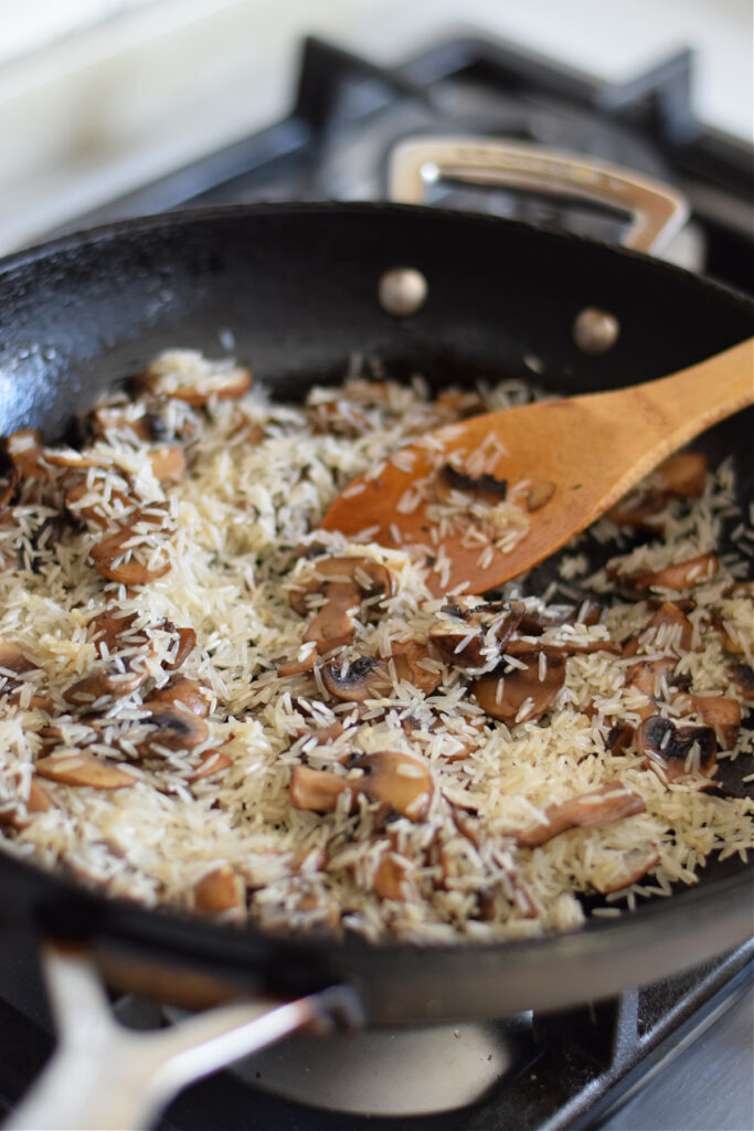 Adding uncooked rice to mushrooms in a skillet.