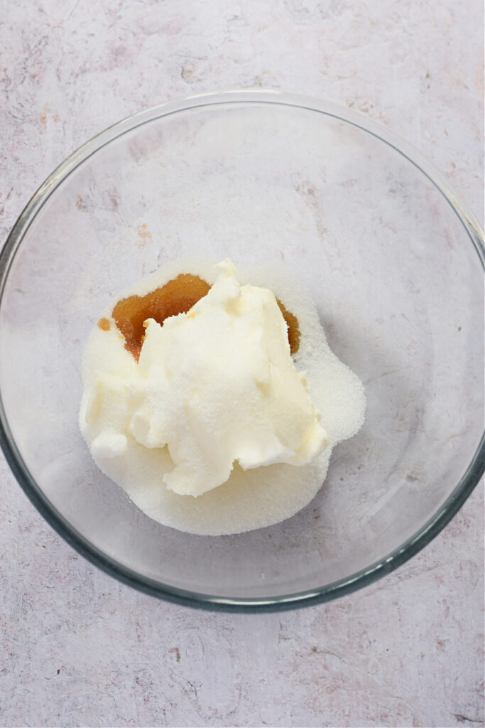 Cream cheese with sugar and vanilla extract in a glass bowl.