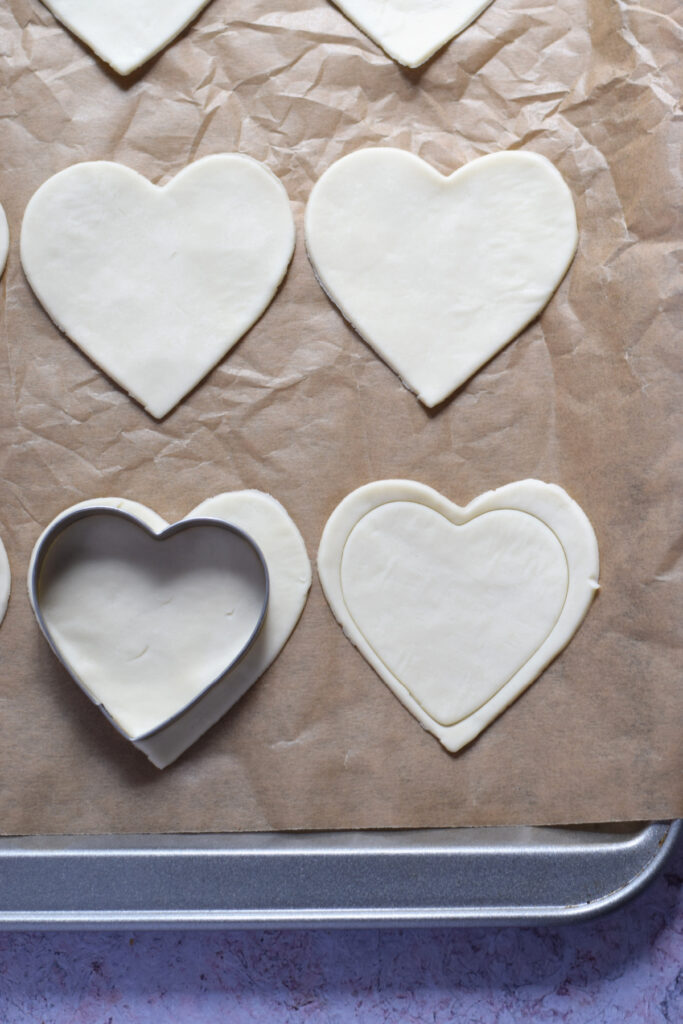 Unbaked puff pastry hearts on a baking tray.