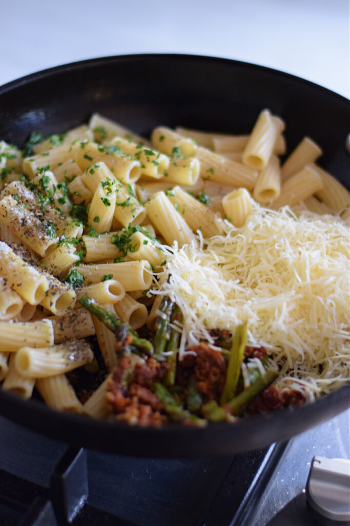 Adding pasta to a skillet to make a asparagus pasta dish.