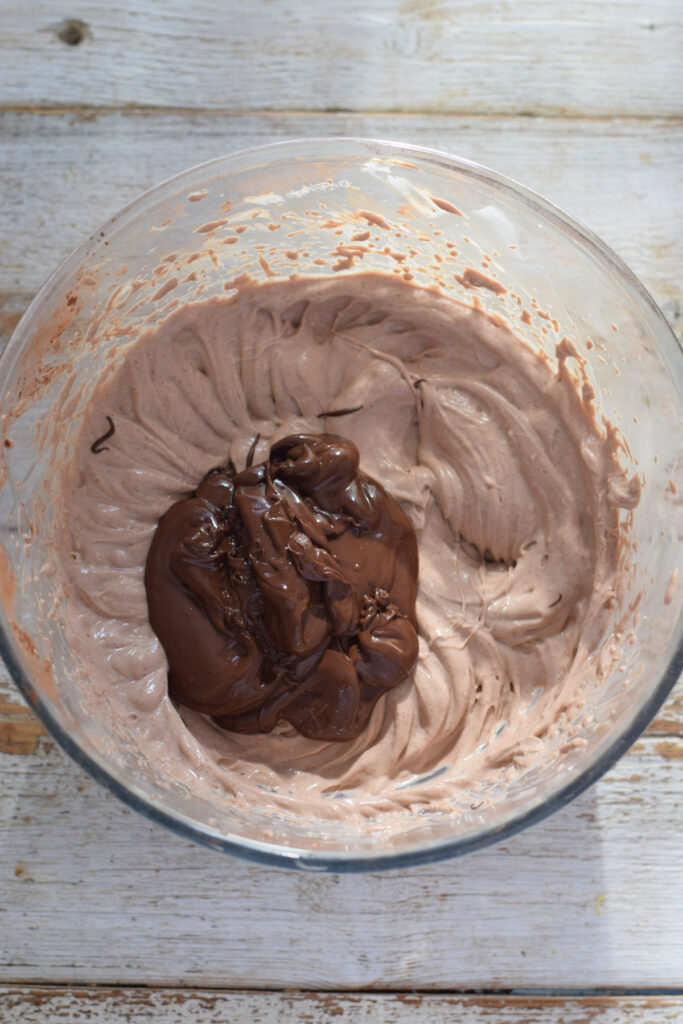 Adding melted chocolate to a cream cheese mixture.