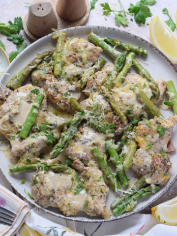 Lemon chicken thighs on a plate with asparagus.