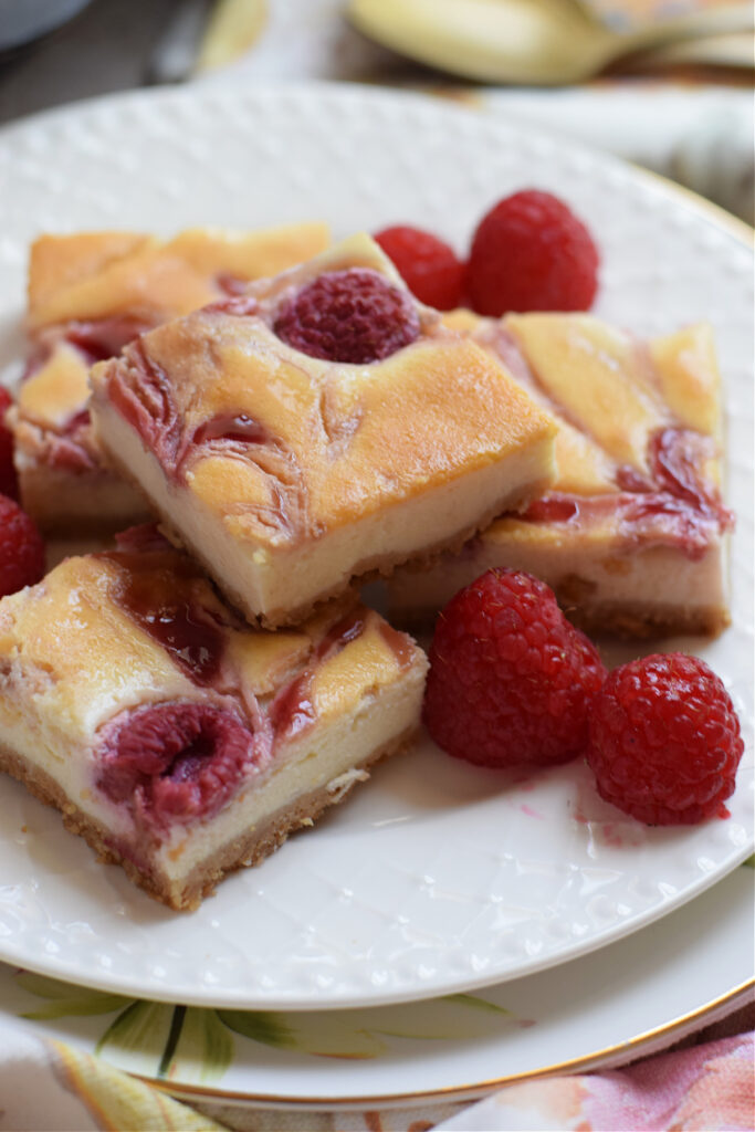 Close up of raspberry cheesecake bars on a white plate.
