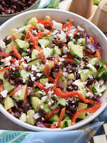Cucumber feta and black bean salad in a white bowl.