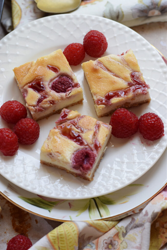 Close up of raspberry cheesecake bars on a white plate.
