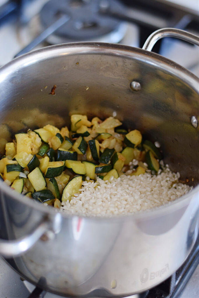 Adding rice to cooked zucchini in a pot.