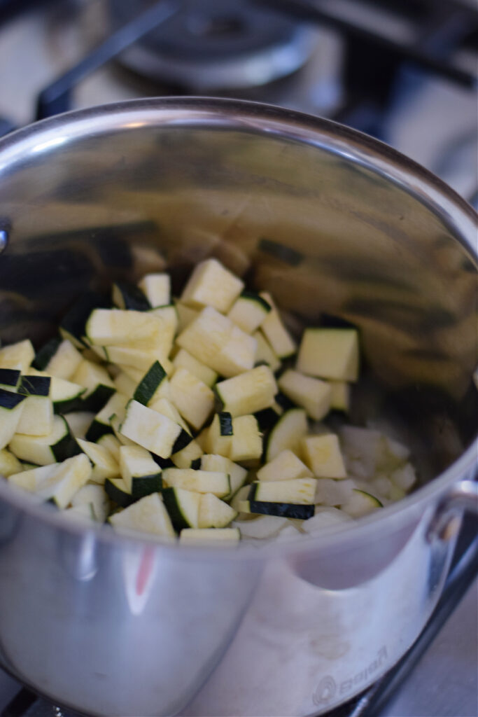 Adding zucchini and onion to a pot.