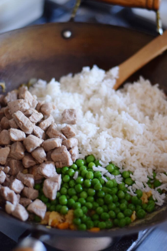 Adding rice, peas and pork to a wok.