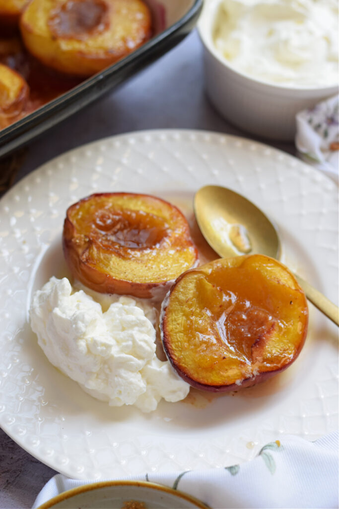 Baked peaches on a white plate with whipped cream.
