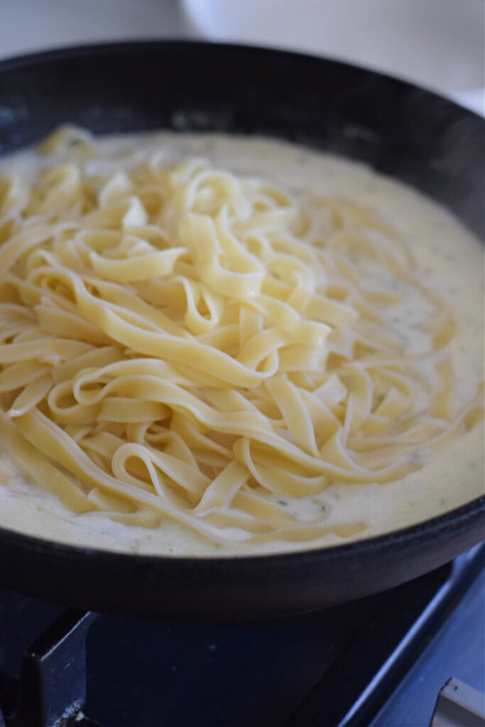 Adding tagliatelle to creamy sauce.